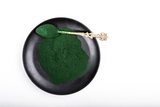 An isolated tablespoon of dried organic spirulina algae powder, on white or rustic background.