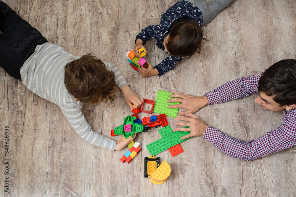 Wall mural top view of father with his two children brother and sister they are playing with plastic toy buildi