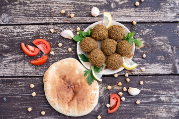 falafel balls from hummus the plate with design lemon and parsley, tomato, garlic on wooden table background with cilantro Vegetarian dish -  from spiced chickpeas food flat lay