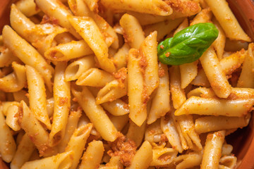 Macarrones con pesto rojo y una hoja de albahaca fresca.