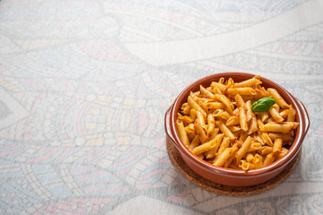 Cazuela de barro con macarrones al pesto rojo sobre fondo blanco