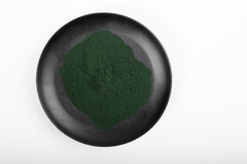 An isolated tablespoon of dried organic spirulina algae powder, on white or rustic background.