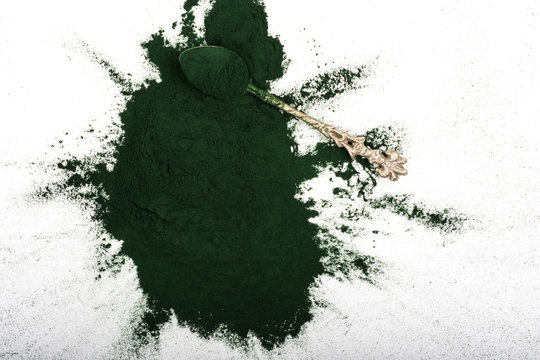 An isolated tablespoon of dried organic spirulina algae powder, on white or rustic background.