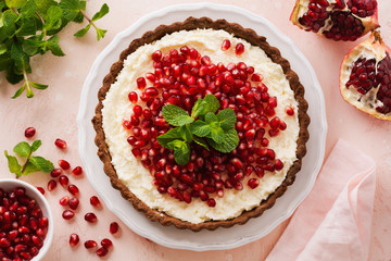 Homemade dessert chocolate tart with coconut cream and pomegranate and mint on a pink table background. Top view.