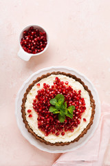 Homemade dessert chocolate tart with coconut cream and pomegranate and mint on a pink table background. Top view.