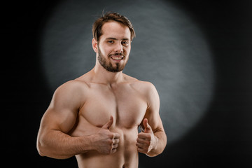 Fototapeta na wymiar A handsome muscular man without a t-shirt poses for a photographer in a dark photo Studio. The concept of sport