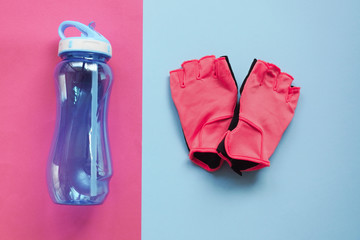 Flat lay pink sports Weight Training gloves for a Bicycle or gym lie on a blue background. Reusable blue water bottle on a blue background. Concept of sports and a healthy lifestyle. Jogging or yoga