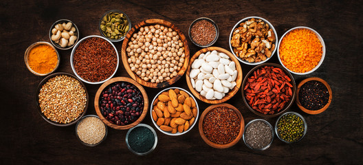 Superfoods, legumes, nuts, seeds and cereals set in bowls on wooden background. Superfood as chia, spirulina, beans, goji berries, quinoa, turmeric, mung bean, buckwheat, lentils, flax seed, wild rice