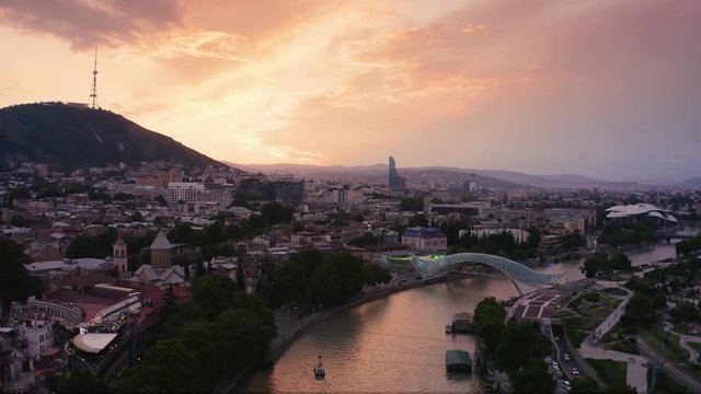 The evening panorama and flight over of the old town in the old district of Avlabari, Holy Trinity Cathedral and Rike Park, the Kura river reflects the evening city lights in Tbilisi, Georgia.