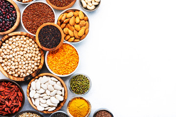 Various superfoods, legumes, cereals, nuts, seeds in bowls on white background. Superfood as chia, spirulina, beans, goji berries, quinoa, turmeric, mung bean, buckwheat, lentils, flax seed, wild rice