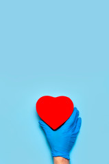 Men's hands in blue medical gloves hold red heart on blue background Flat lay. Concept of saving lives and maintaining health. Doctor's hands with a heart symbol. Medicine, cardiology, love of life