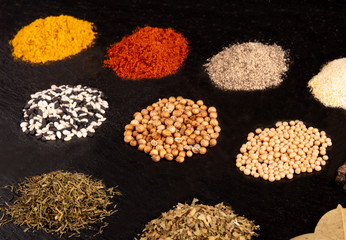 Different piles of spices isolated on black stone plate plaque. Place for text copy space.