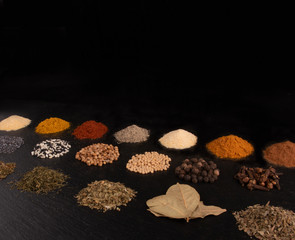 Different piles of spices isolated on black stone plate plaque. Place for text copy space.