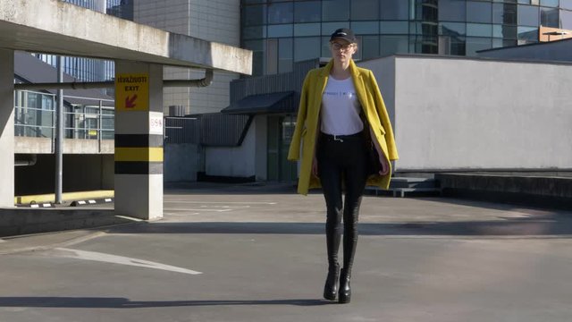 Confident supermodel with high heels walks on the roof of parking lot, wears feminist sings