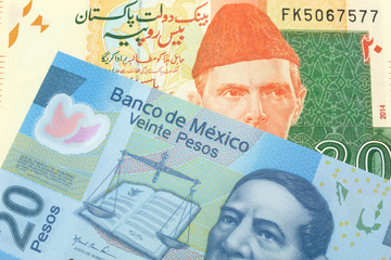 An orange and green twenty Pakistani rupee bank note with a red one hundtwenty Mexican peso bank note in macro
