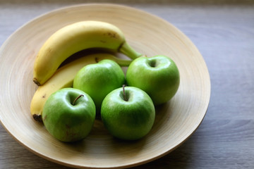 Wooden bowl with green apples and bananas on a table. Selective focus.