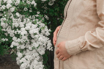 pregnant woman outdoors hugging her stomach on the background of flowers 