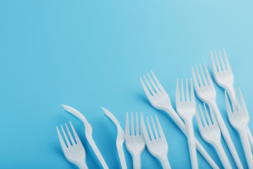 White plastic forks of disposable tableware on a blue background.
