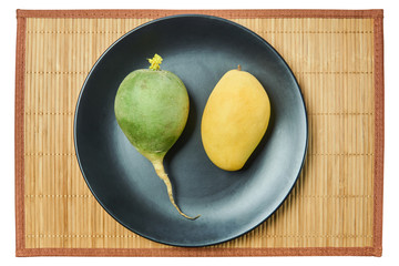 green radish and yellow mango on a gray plate on a cane tablecloth