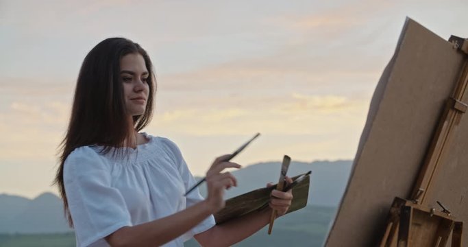 Caucasian female artist relaxing on top of mountain, creating a picture of sunset lake - inspirational landscape, recreational pursuit concept 4k footage