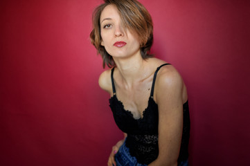 Young woman with short hair dressed in black lace bustier and blue jeans is posing in the studio on bright pink background