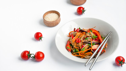 Hot Korean-style eggplant and tomato salad with sesame seeds and herbs on a white table. Asian food. Vegetarian dish.
