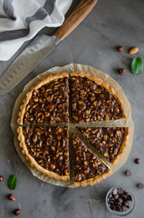 Tart with chocolate caramel, hazelnuts, peanuts, almonds and seed mix on a dark concrete background. Vertical orientation. Top view.