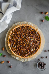 Tart with chocolate caramel, hazelnuts, peanuts, almonds and seed mix on a dark concrete background. Vertical orientation. Top view.