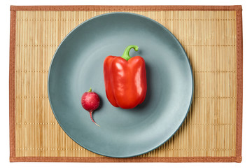small pink radish and big red bell pepper on a gray plate on a cane tablecloth