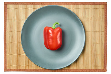 red bell pepper on a gray plate on a cane tablecloth