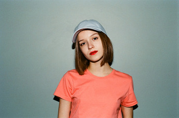 Vintage photo with grain on film camera, girl in stylish casual clothes stands on gray wall...