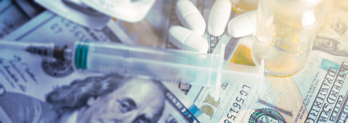 Medicine and money. Vials of antibiotics, white anti-virus tablets, and a medical syringe with a...