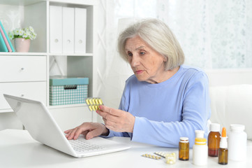 Ill beautiful senior woman with pills using laptop