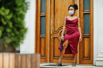 Covid-19, infectious virus. African woman with curly hair, wears red silk dress and medical disposable mask, cares about her health and protects in dangerious situation.