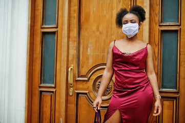 Fototapeta na wymiar Covid-19, infectious virus. African woman with curly hair, wears red silk dress and medical disposable mask, cares about her health and protects in dangerious situation.