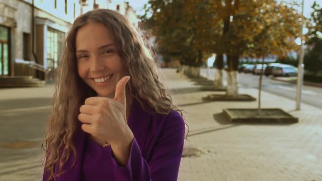 Smiling curly long haired girl gives shows thumbs up. Like gesture. Big toe finger. Woman without makeup beauty products cosmetic care. Fashionable stylish woman. Vogue business lady looks into camera