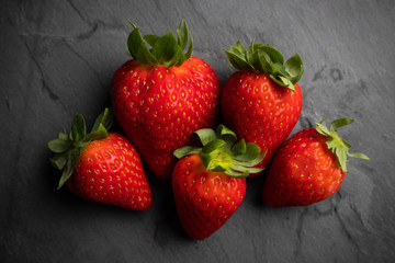 five strawberries on a black stone background, dark food photography