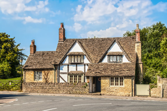 Old half-timbered house with multiple chimneys close  road in to a road in the Cotswolds UK