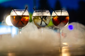 Beautiful row line of different colored alcohol cocktails on a party, martini, vodka,and others on decorated catering bouquet table on open air event, picture with beautiful bokeh