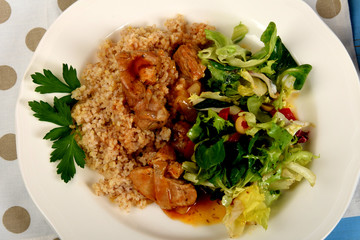 A piece of meat on cooked barley and green lettuce with additions