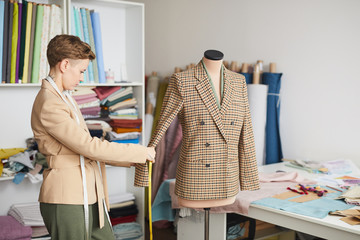 Young fashion designer taking measurements from the jacket with tape measure in the workshop
