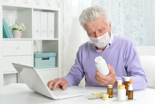 Ill senior man with facial mask using laptop