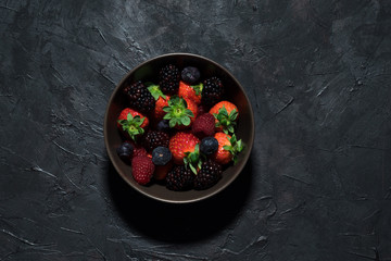 Bowl of red fruits on a black rustic surface. Top view. Healthy food.