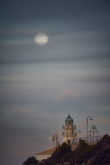 Moon eclipse over a lighthouse on the coast