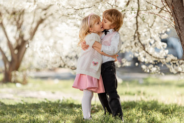 Happy sister and brother are playing in blossom cherry garden outdoors.