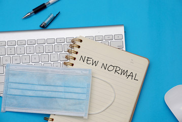"New Normal" writing on a book with a keyboard and mask on a blue background, New Normal concept.