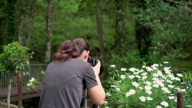A young girl, a photographer, in a forest area, takes pictures of flowers and beautiful nature.