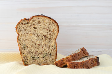 Baked bread with seeds on kitchen towel. Wooden background. Copy space, empty place. Sliced brown bread.