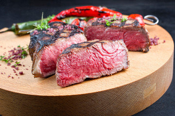 Barbecue dry aged wagyu roast beef steak with tomatoes and chili as closeup on a modern design...