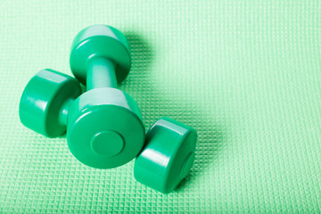 Green dumbbells on a fitness carpetю Dumbbells on green with copy space.